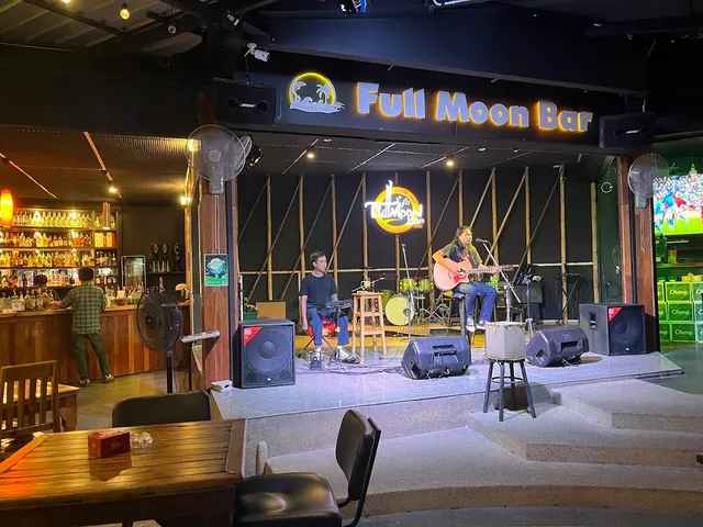 A singer with a guitar and a keyboard player on stage, beside a bar counter with bottle shelves