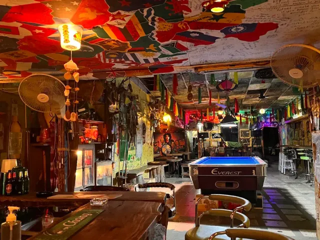 A ceiling covered in colorful flags, a pool table and a wooden counter beside it