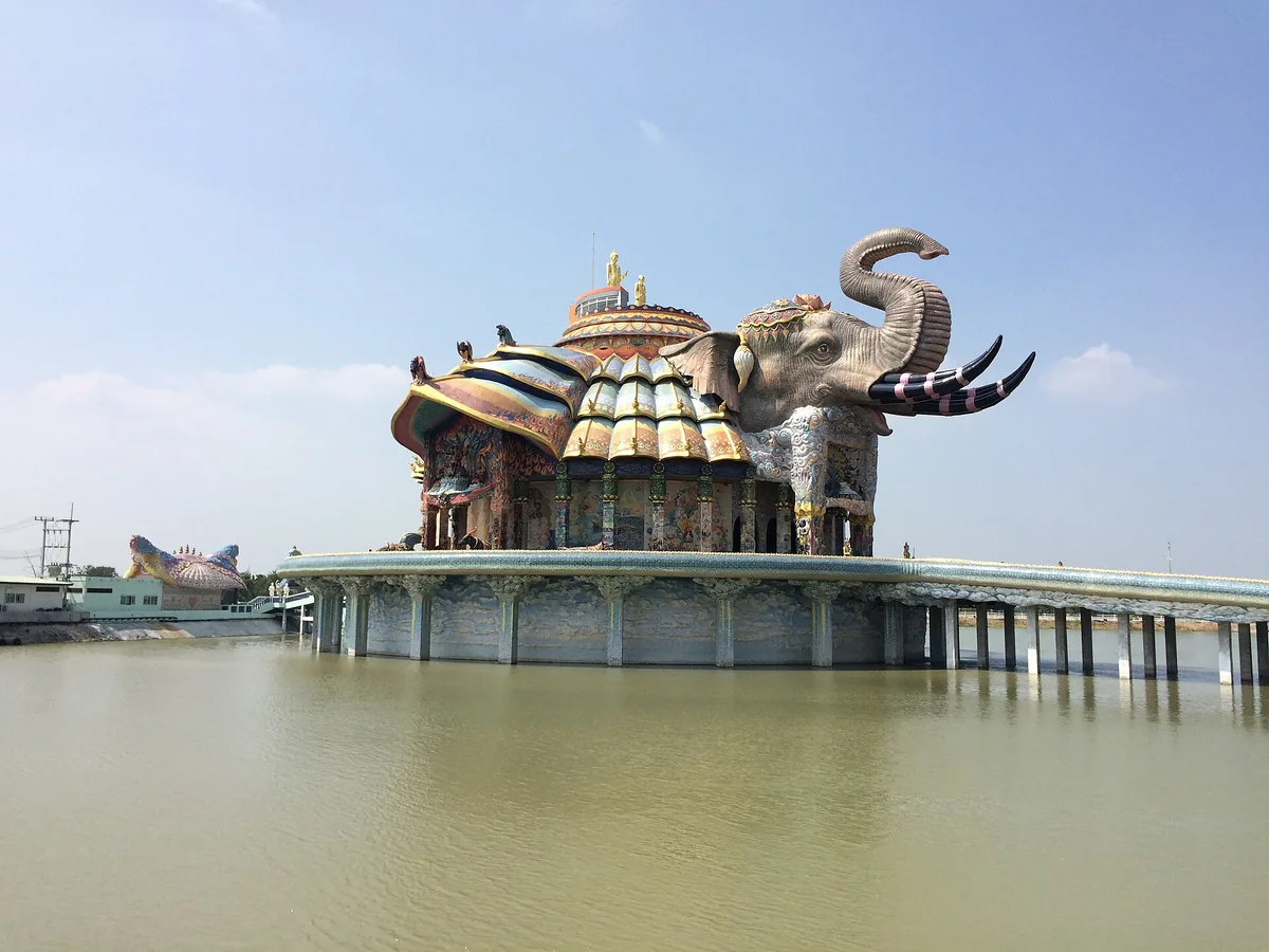 Giant elephant shaped temple with a raised trunk and tusks standing on pillars above a lake