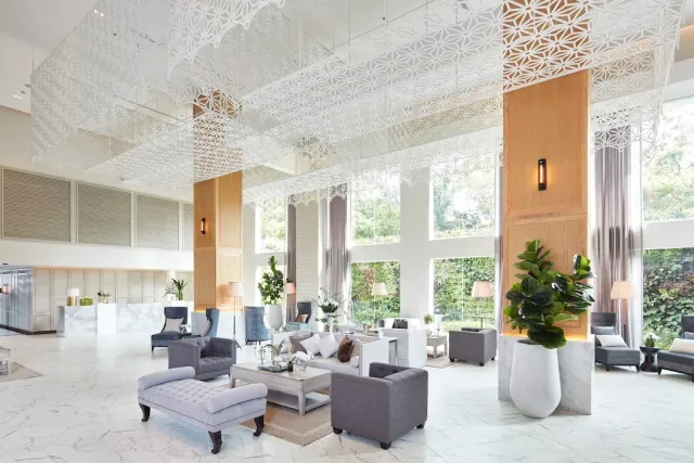 A bright lobby with gray armchairs, a white lattice ceiling and potted plants