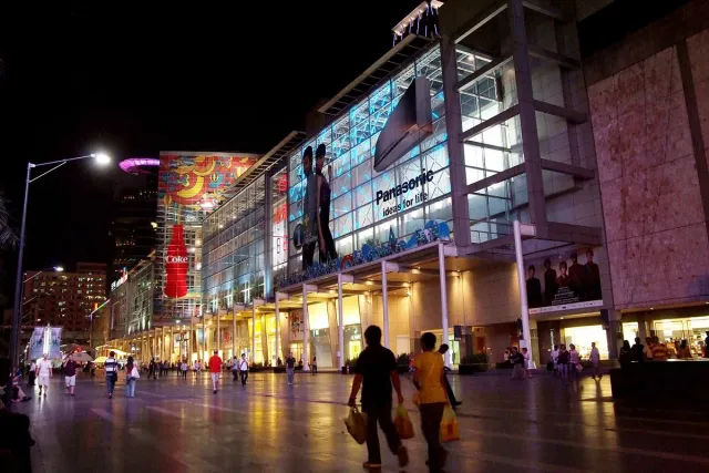 The lit glass frontage of a large shopping centre along a city street in the evening