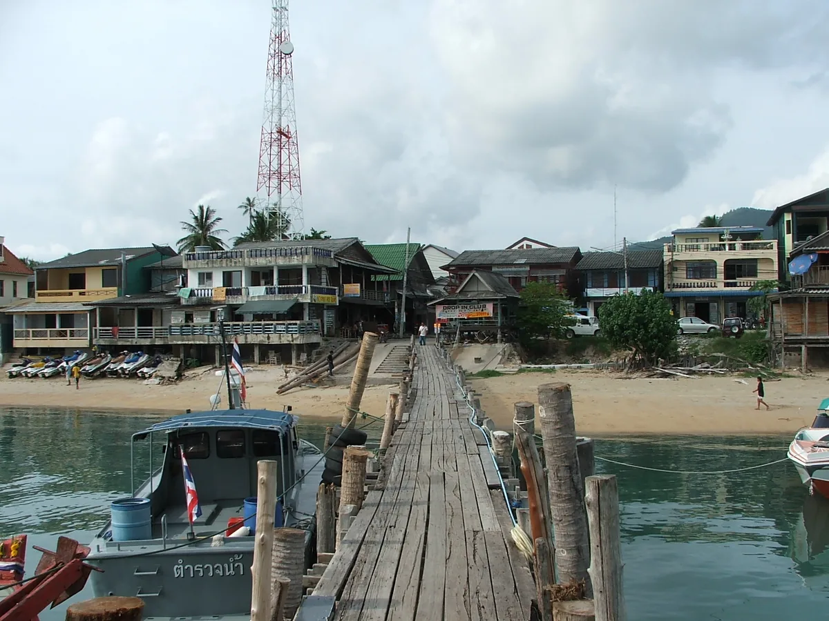 Long wooden pier leading to timber houses on the shore with fishing boats moored on both sides
