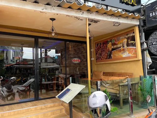 An open business front with a large dish banner, wooden benches and motorbikes parked outside