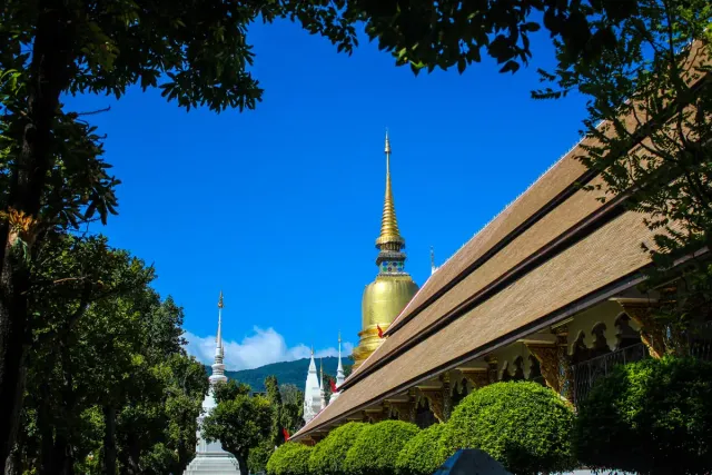 A gilded chedi rising behind a red and gold temple roof against a blue sky
