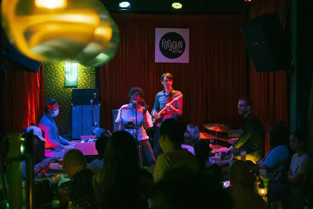 A jazz band with a singer, guitarist and drummer on stage in front of a red curtain