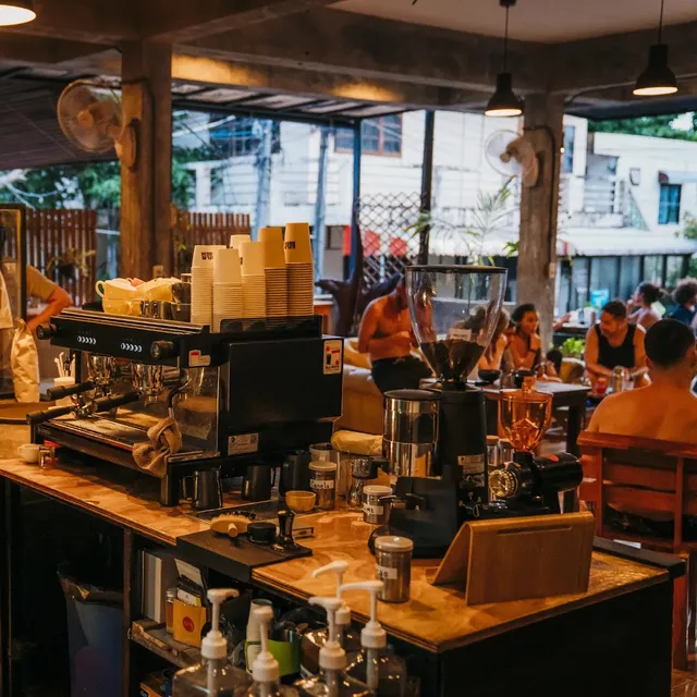 A wooden counter with an espresso machine and coffee grinders facing seated guests