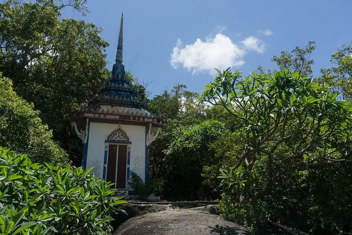 A white temple building with a pointed spire standing among dense tropical greenery