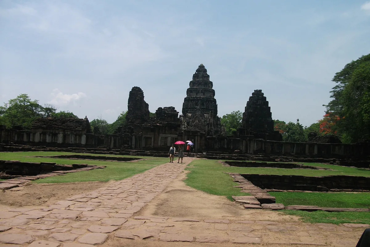 A wide stone causeway leading to a Khmer sandstone sanctuary with tiered towers, between lawns