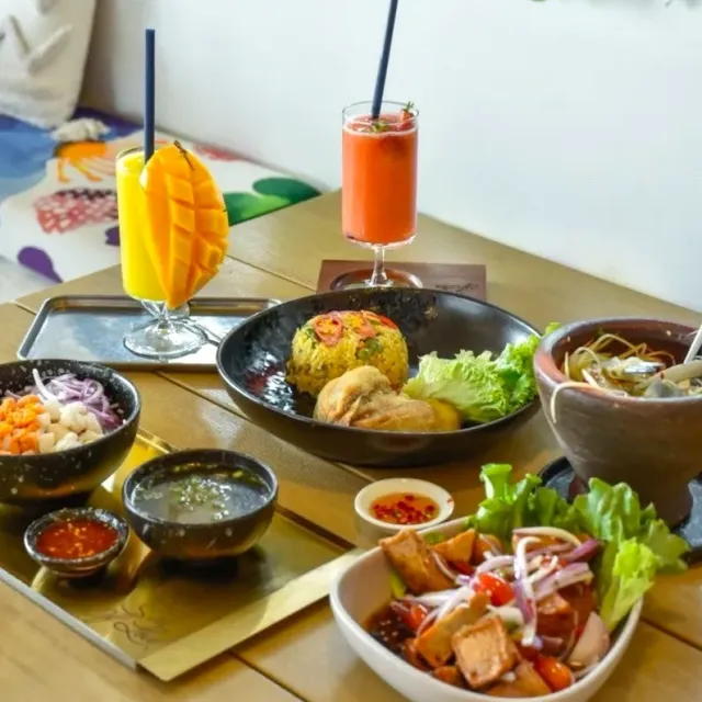 An assortment of dishes in dark bowls with seasoned rice and two fruit drinks in tall glasses