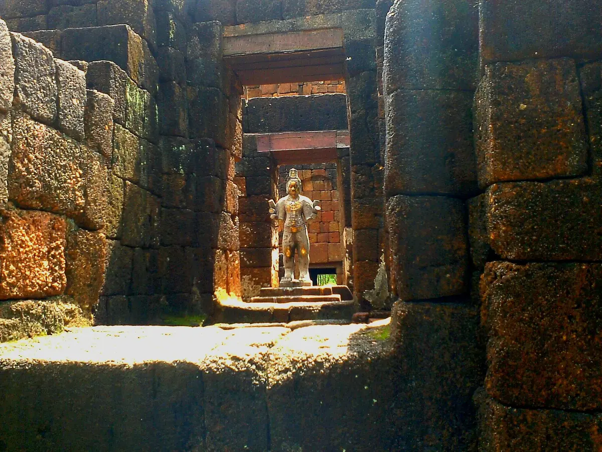 Ancient laterite stone gateway framing a sunlit standing stone figure
