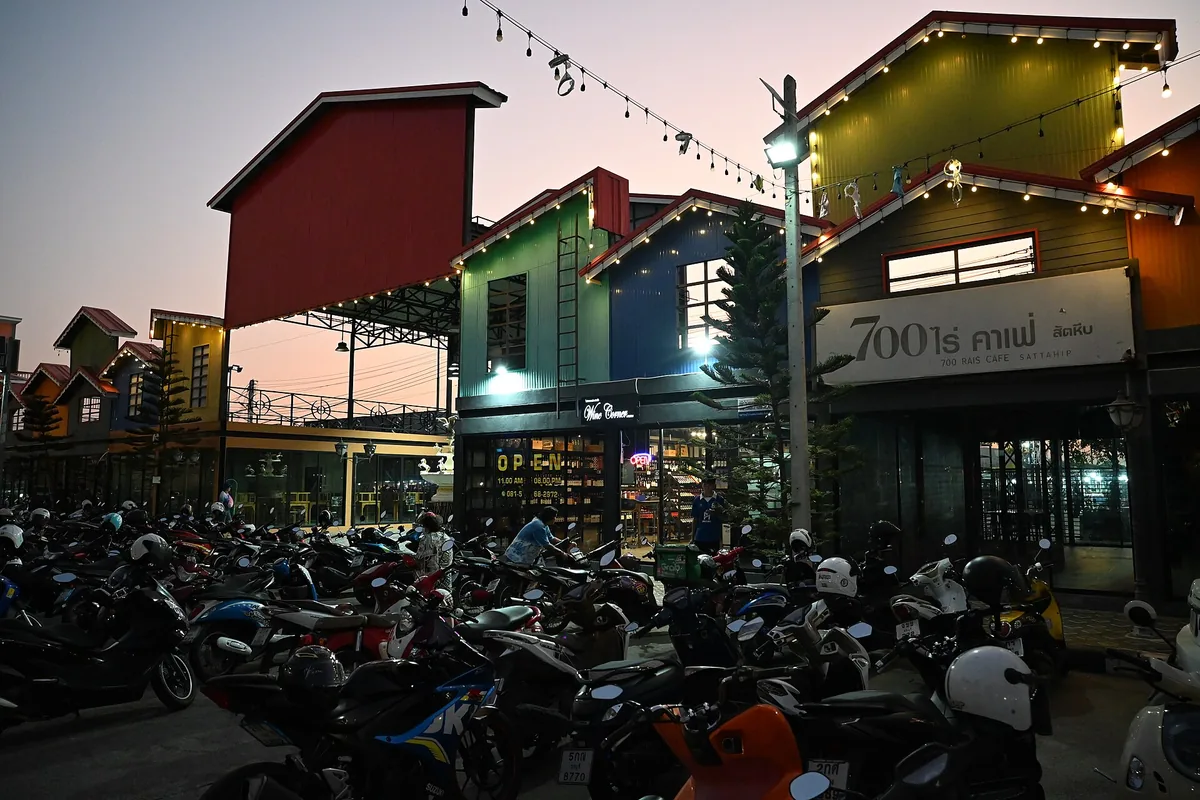 Colourful wooden shopfronts lit by strings of bulbs above rows of parked scooters at dusk