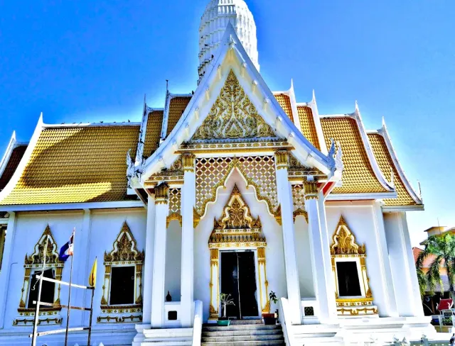 A white temple hall with a yellow roof and gold ornaments, and a white chedi behind it