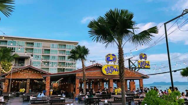 Brick pavilions on the beach with hanging bulbs, palms and tables full of diners
