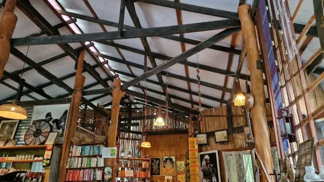 A high wooden beam ceiling above bookshelves, framed pictures and hanging lamps