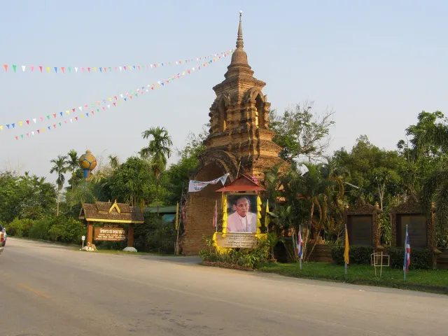An old brick chedi beside a road, strung color pennants and a framed photograph in front