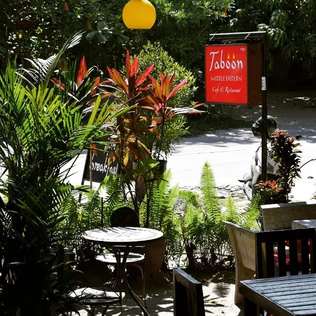A seating corner in a tropical garden with a round table and a hanging red sign