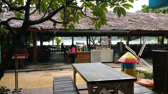 Wooden tables under a thatched roof, with a view of the sea and green hills behind