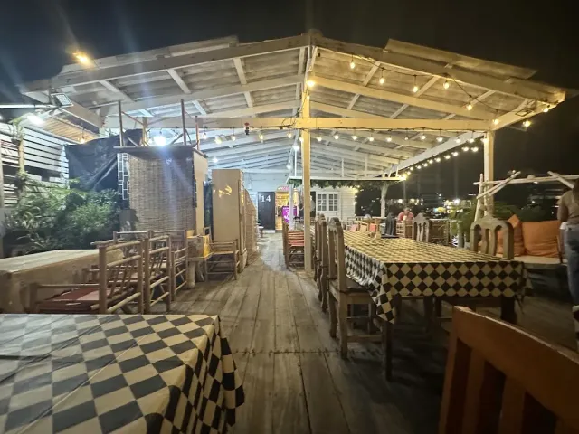 A wooden deck at night with black and white checked tablecloths and bulbs hanging above