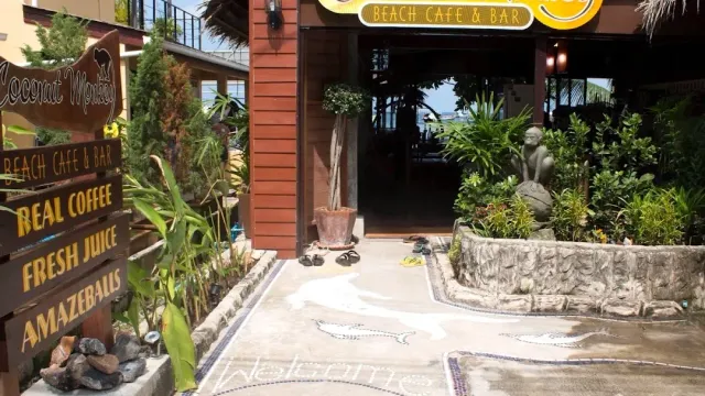 A shaded entrance with wooden signs, greenery, a stone statue and a mosaic floor