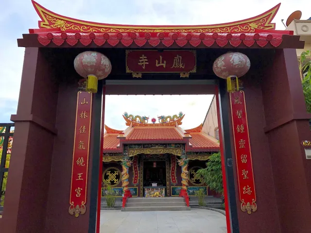 A red Chinese gate with lanterns and gold inscriptions, a decorated temple beyond it