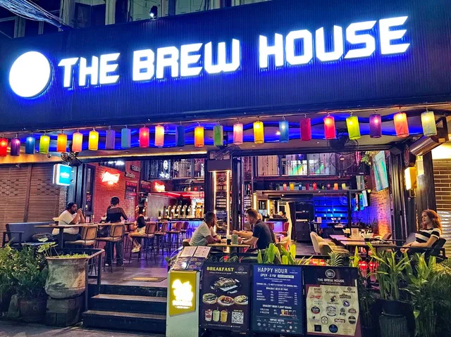 A lit bar frontage in the evening with hanging colorful lanterns and people seated at outdoor tables