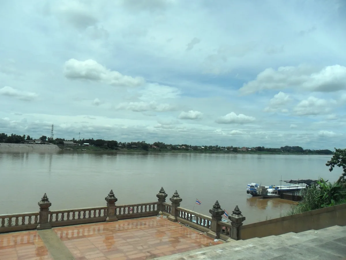 The Mekong promenade at Nong Khai, a stone balustrade along the river and a boat passing