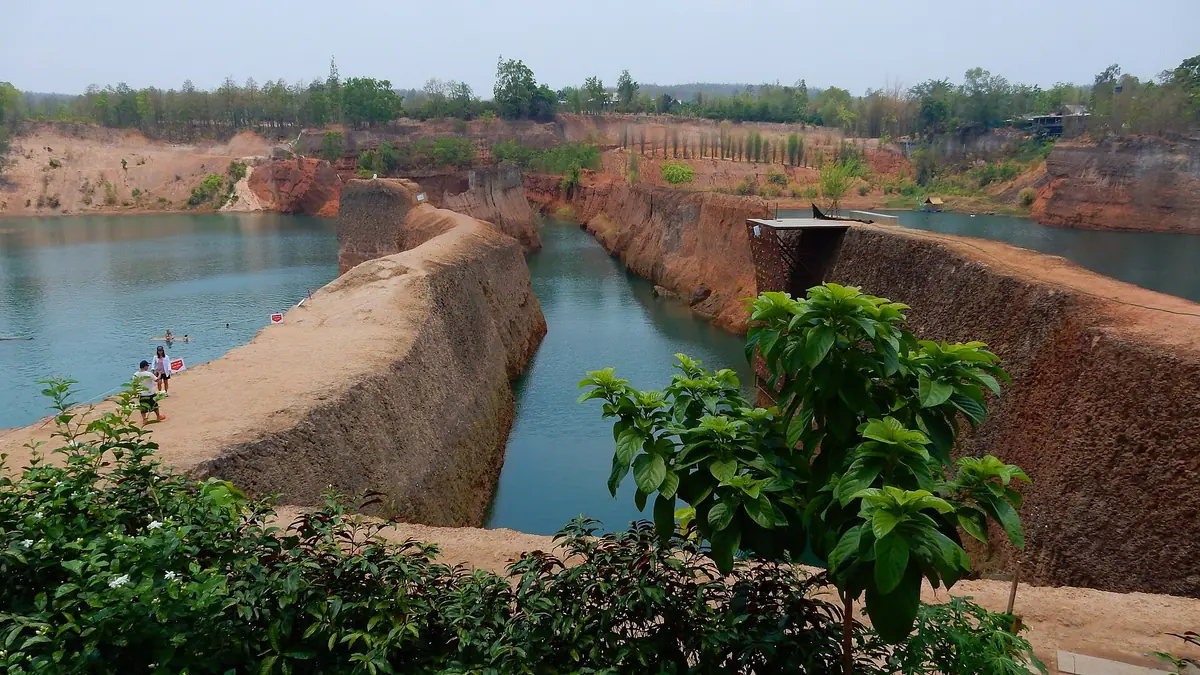 Flooded quarry of turquoise water between red earth ridges with bathers along the edge
