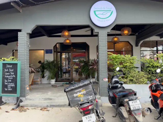 An entrance with a round sign and hanging lamps, a chalkboard and motorbikes out front