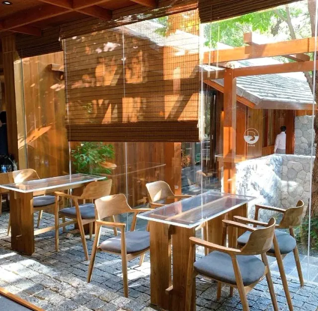 A wooden terrace with glass tables, light chairs and rolled bamboo blinds