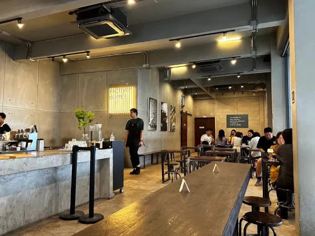 An industrial concrete space with a coffee counter, a long wooden table and stools