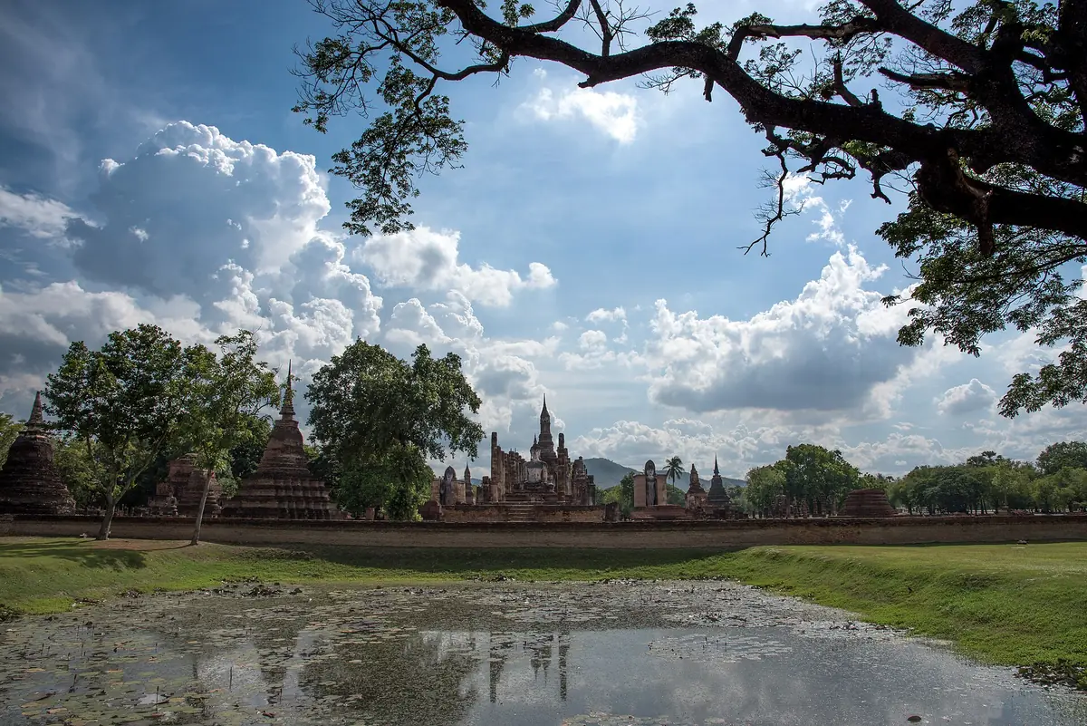 Ancient brick chedis and spires reflected in a pond beneath a cloudy sky
