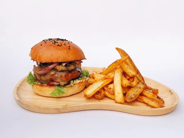 A burger with onion and lettuce beside seasoned fries on a wooden board