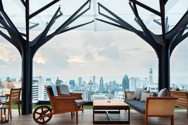 A rooftop seating corner with tree shaped columns and a skyline of towers