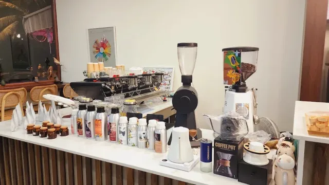 A white counter with an espresso machine, two grinders, kettles and small syrup bottles
