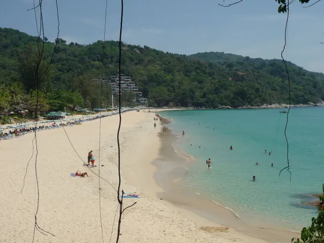 A curving sandy bay with turquoise water and forested hills behind