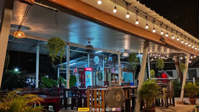 A covered terrace at night with string bulbs hanging and empty wooden tables