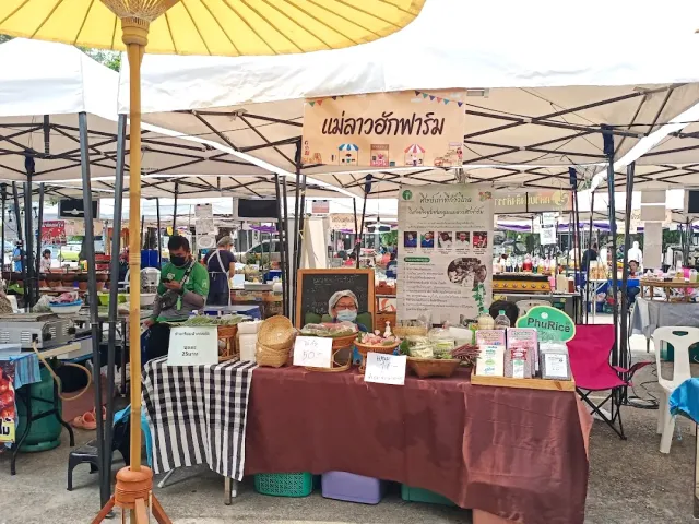 A market stall under white tents and an orange umbrella, vendors and local products