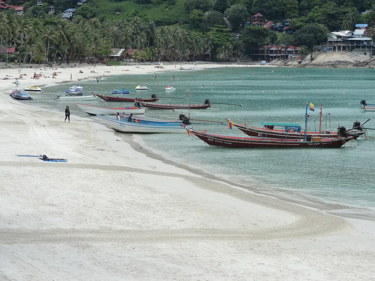 Longtail boats moored in turquoise water along a wide white sand beach