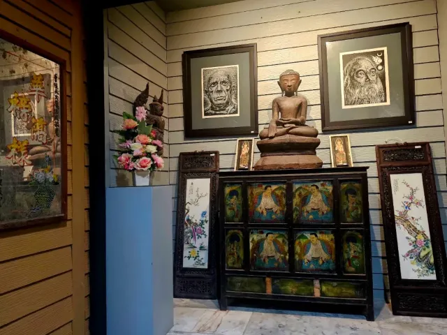 A display room with framed portraits, a wooden Buddha statue and a painted cabinet