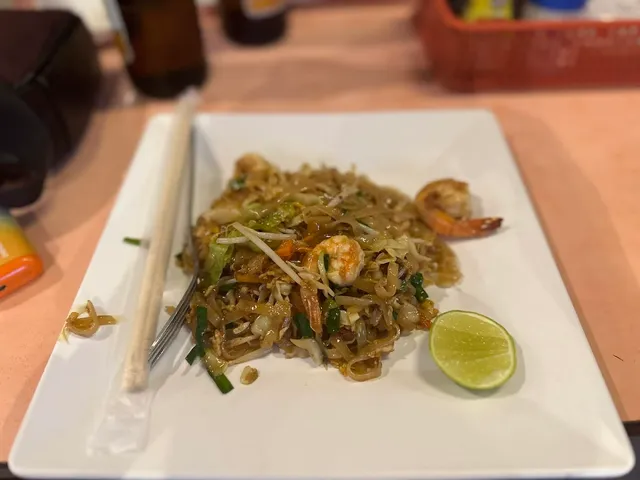 A plate of stir-fried noodles with shrimp and a lime wedge