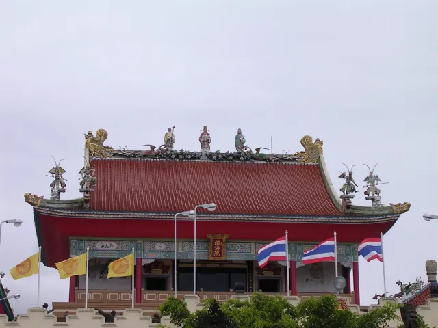 A red Chinese roof decorated with clay figurines and flags fluttering below it