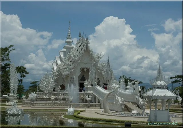An all white temple covered in dense carvings and mirror fragments, ringed by a bridge and statues
