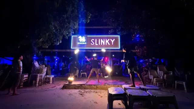A fire dancer on a sand stage at night, beneath a blue lit sign