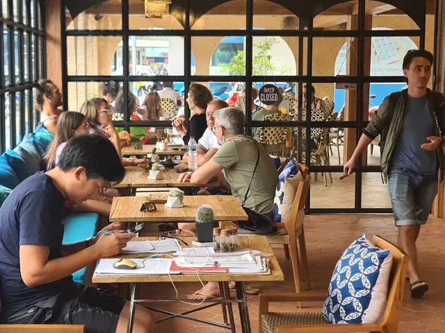 Guests sitting at wooden tables with papers and drinks, facing wide windows