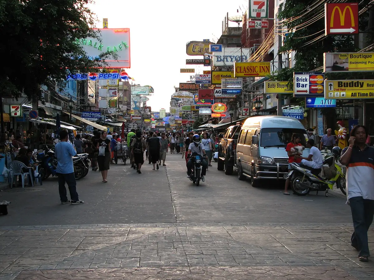 A long street crowded with guesthouse and bar signs on both sides, with pedestrians, motorbikes and a minibus