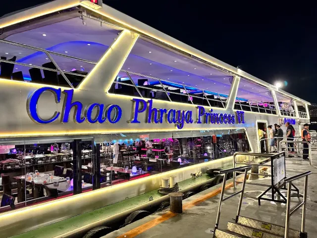 A blue lit cruise boat with set tables, moored beside a pier at night