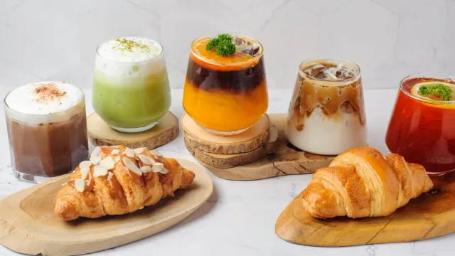 Five drinks in glass cups on wooden boards, beside two croissants