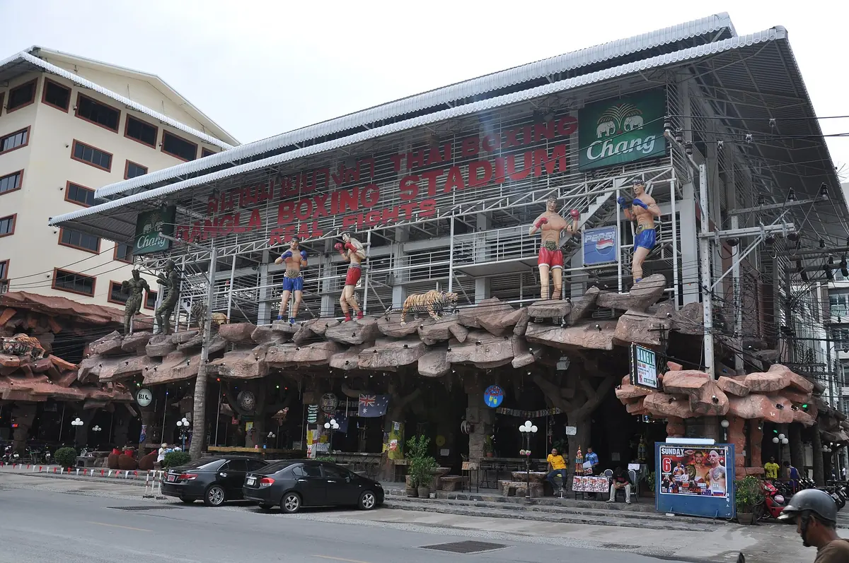 The front of the Bangla Boxing Stadium in Patong, with its red sign and Muay Thai fighter figures on the rocks at the entrance