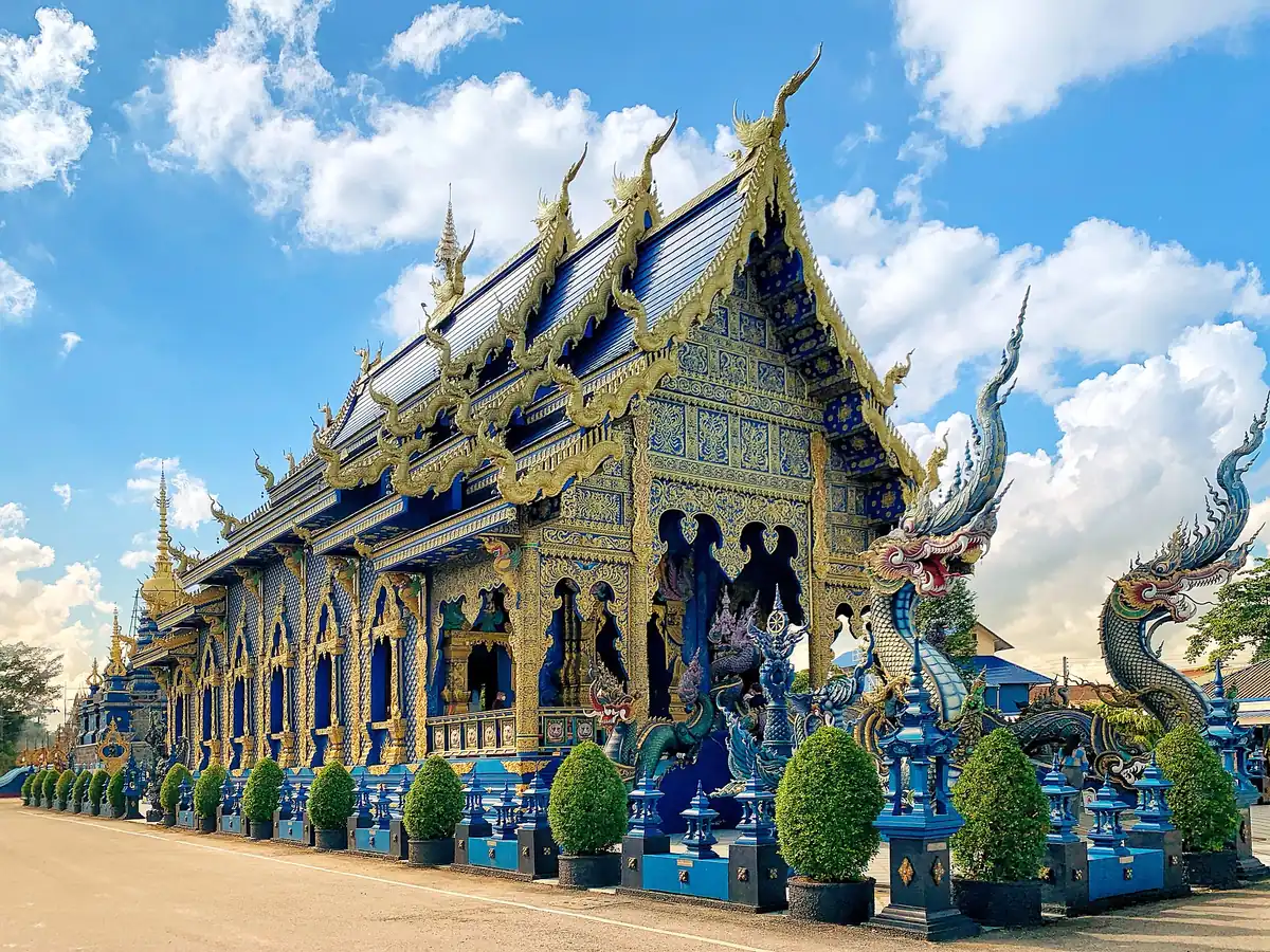 A cobalt blue and gold temple hall with tiered roofs and naga serpent statues at the entrance