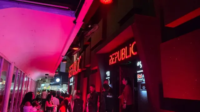 A facade lit in red light with signs, and people standing at the entrance at night